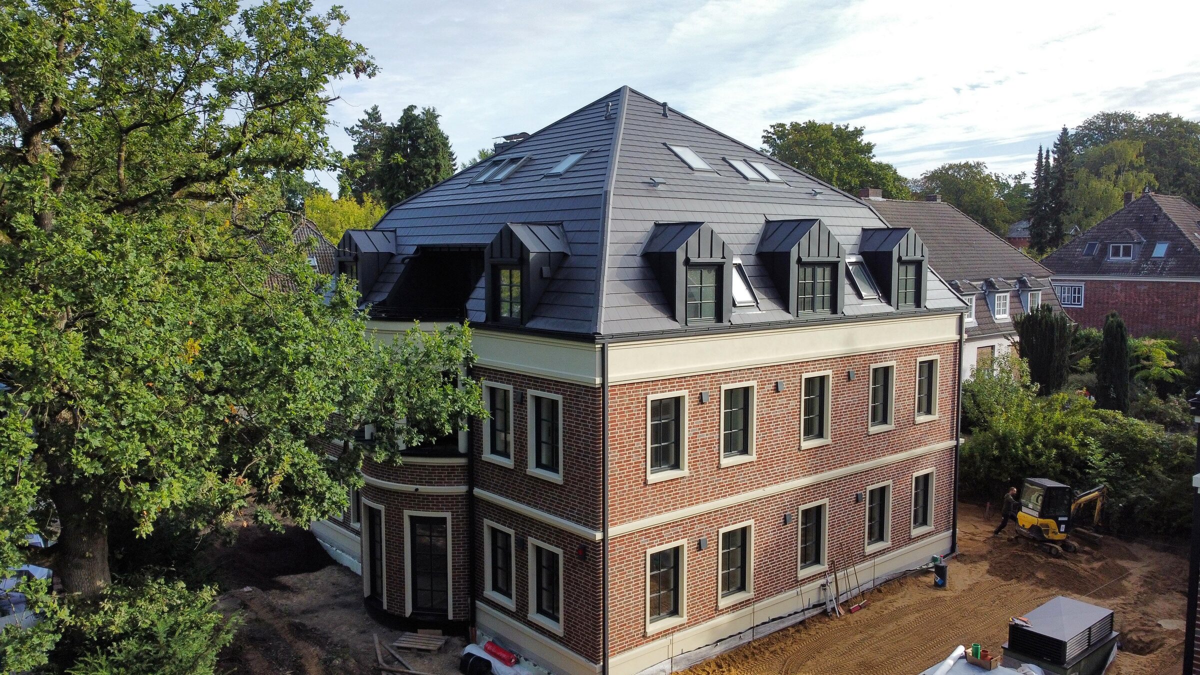 Drohnenfoto vom Oktober 2026: eine der Villen mit Mansarddach, Gauben und Klinkerfassade neben einer alten Eiche